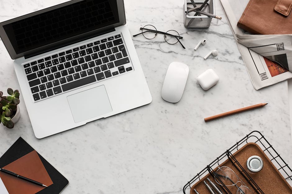 Discover a clean, organized workspace featuring a laptop, AirPods, and stationery essentials on a marble desk.